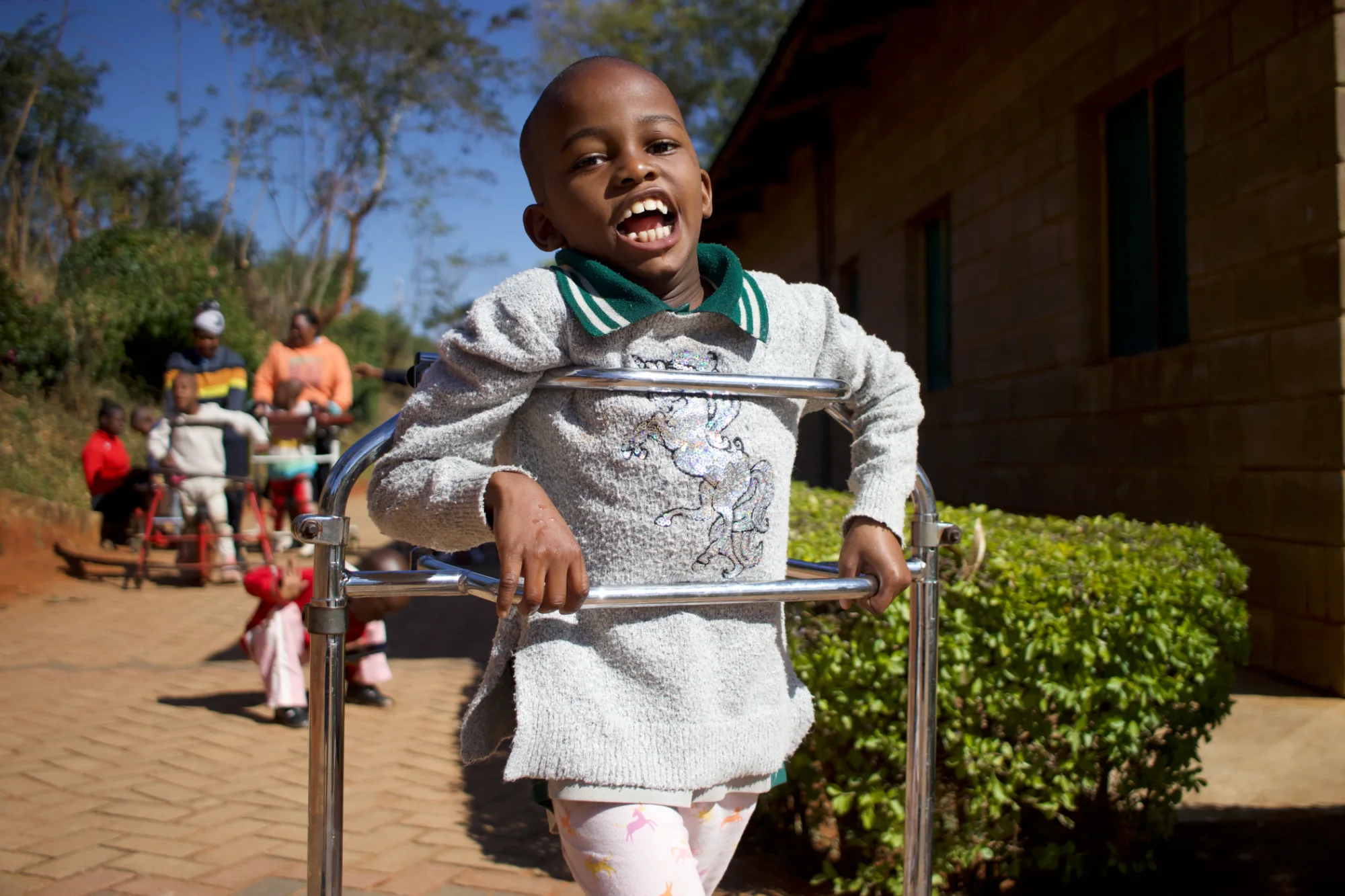A girl grinning as she walks with a frame on the brick path at the Centre